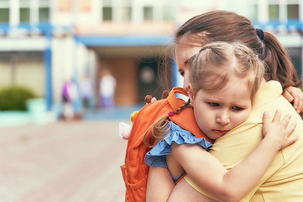 Child hugging mother goodbye at school. Experiencing feelings of separation.